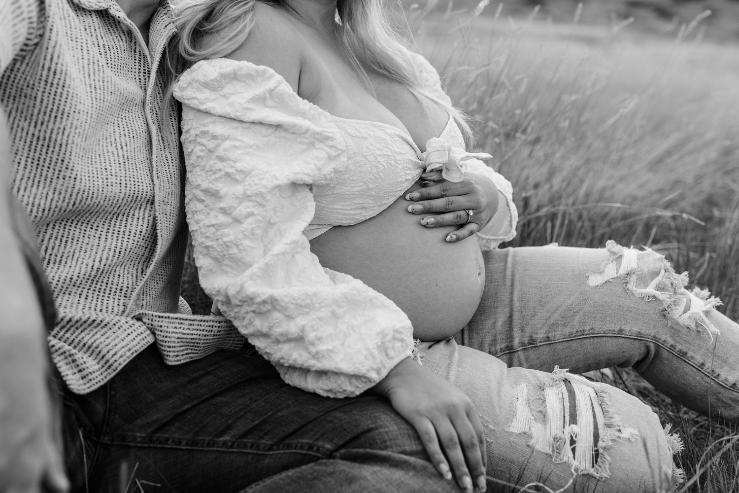 Intimate maternity photoshoot captured in a rustic outdoor setting with golden light and tall grass.