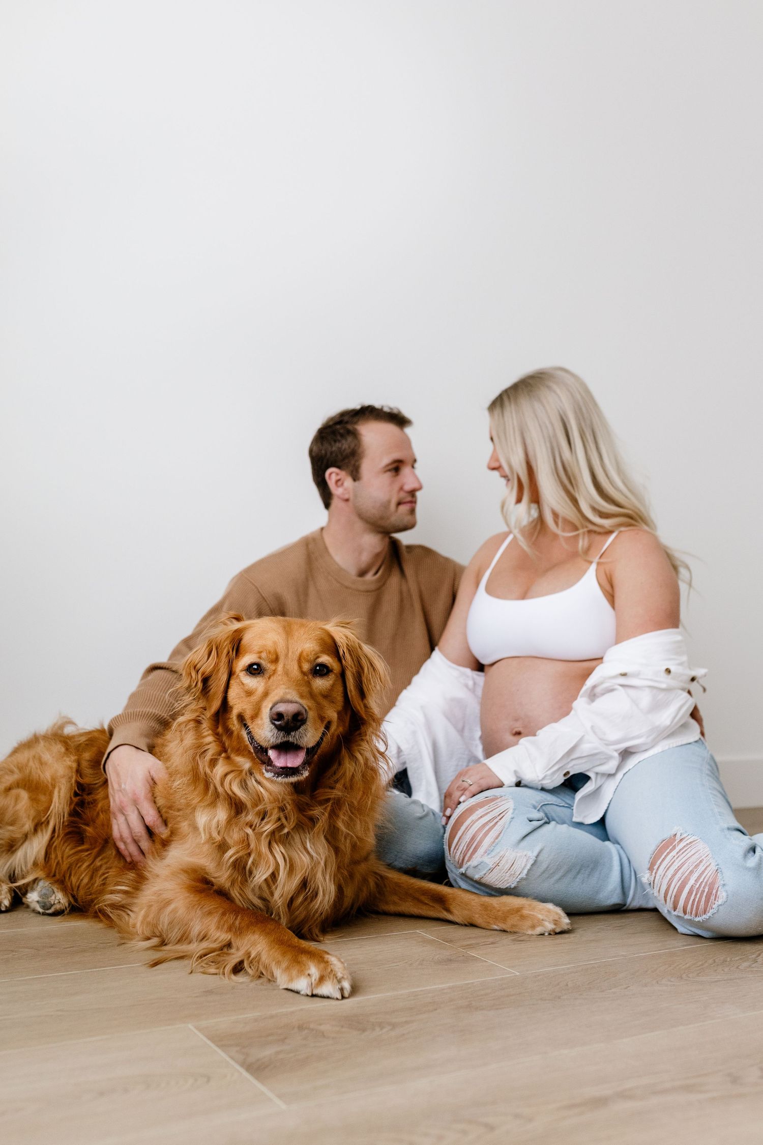 Couple lounging on floor with happy golden retriever in bright studio setting.