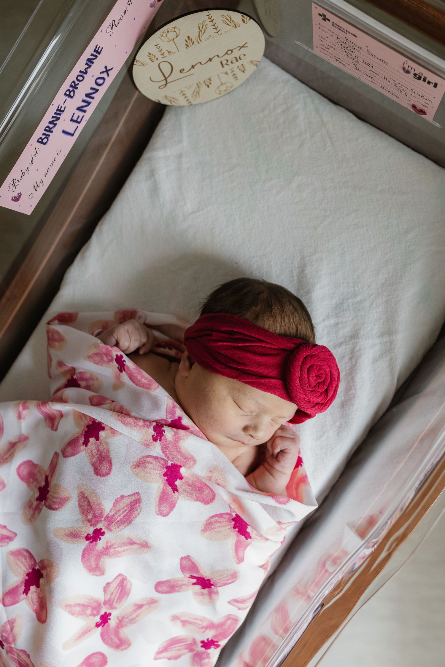 Sleeping newborn wrapped in white blanket with pink butterfly patterns in hospital bassinet.