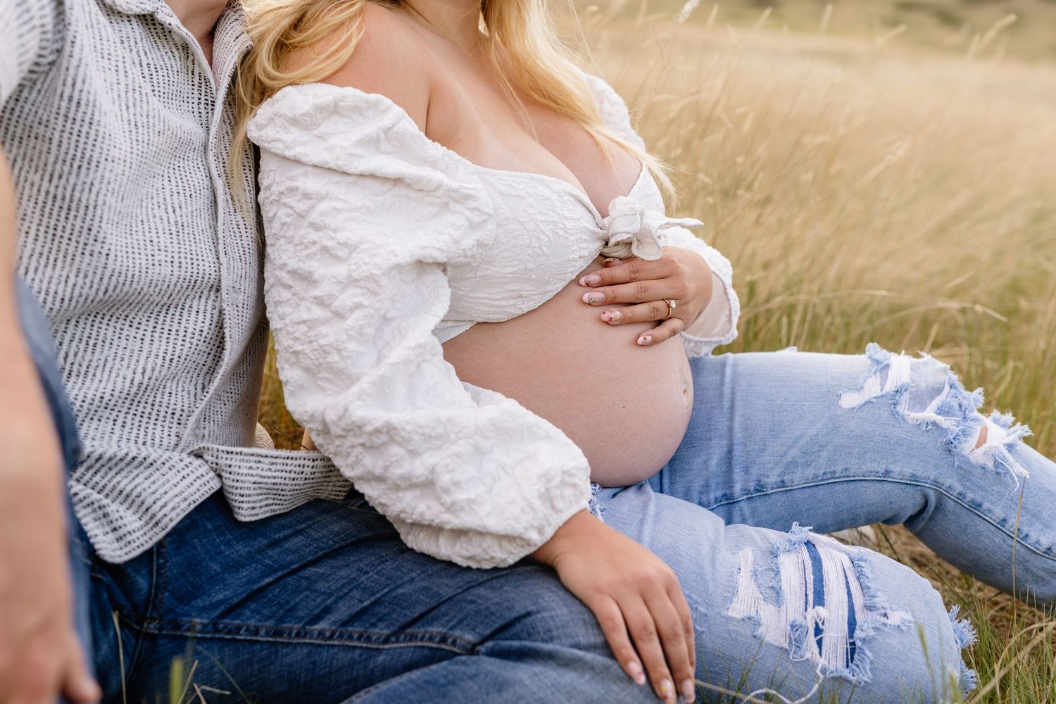 Romantic maternity session in a sun-drenched field with soft natural lighting.