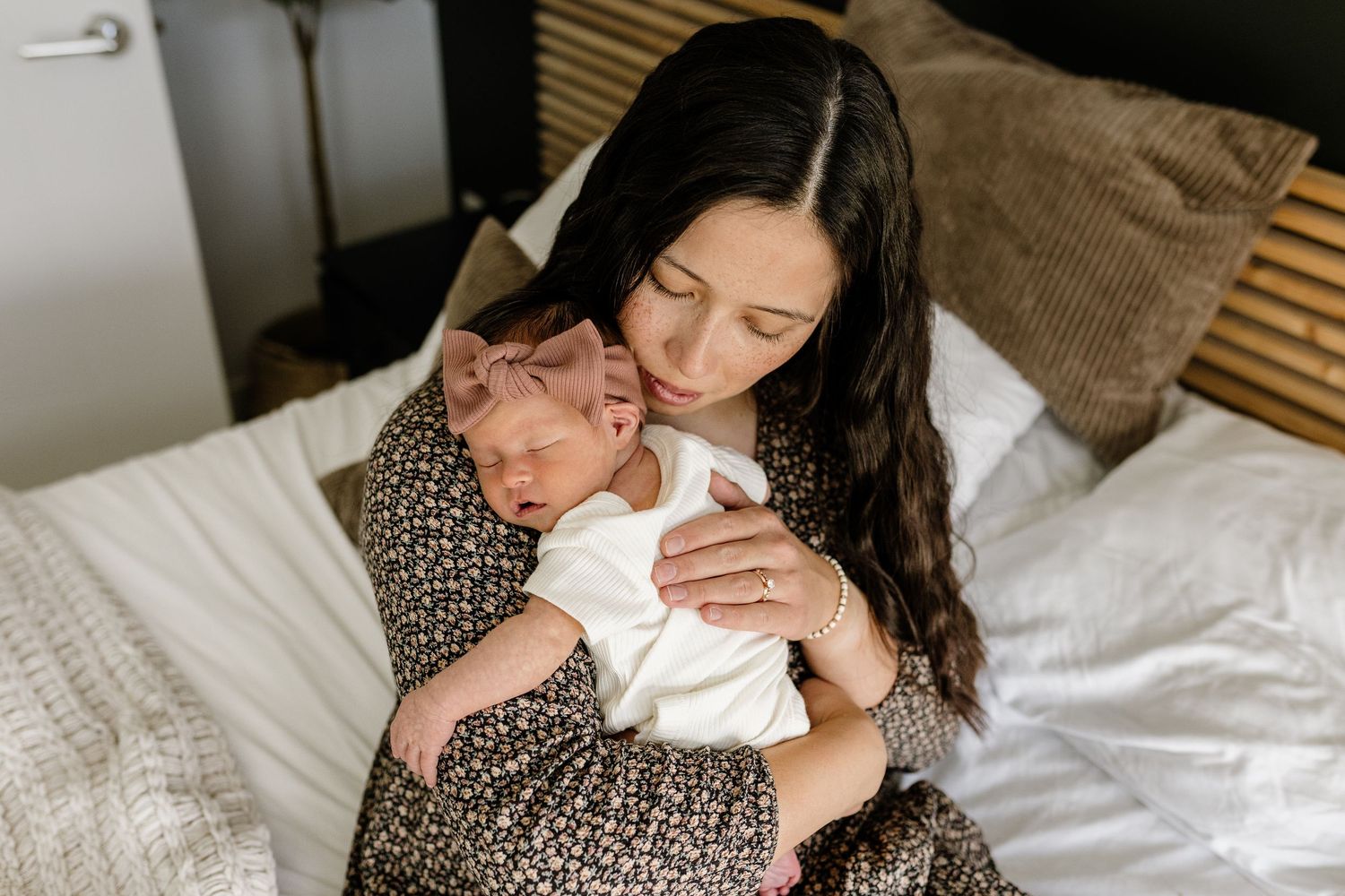 Tender moments captured of parent and newborn baby bonding together on white bedding.