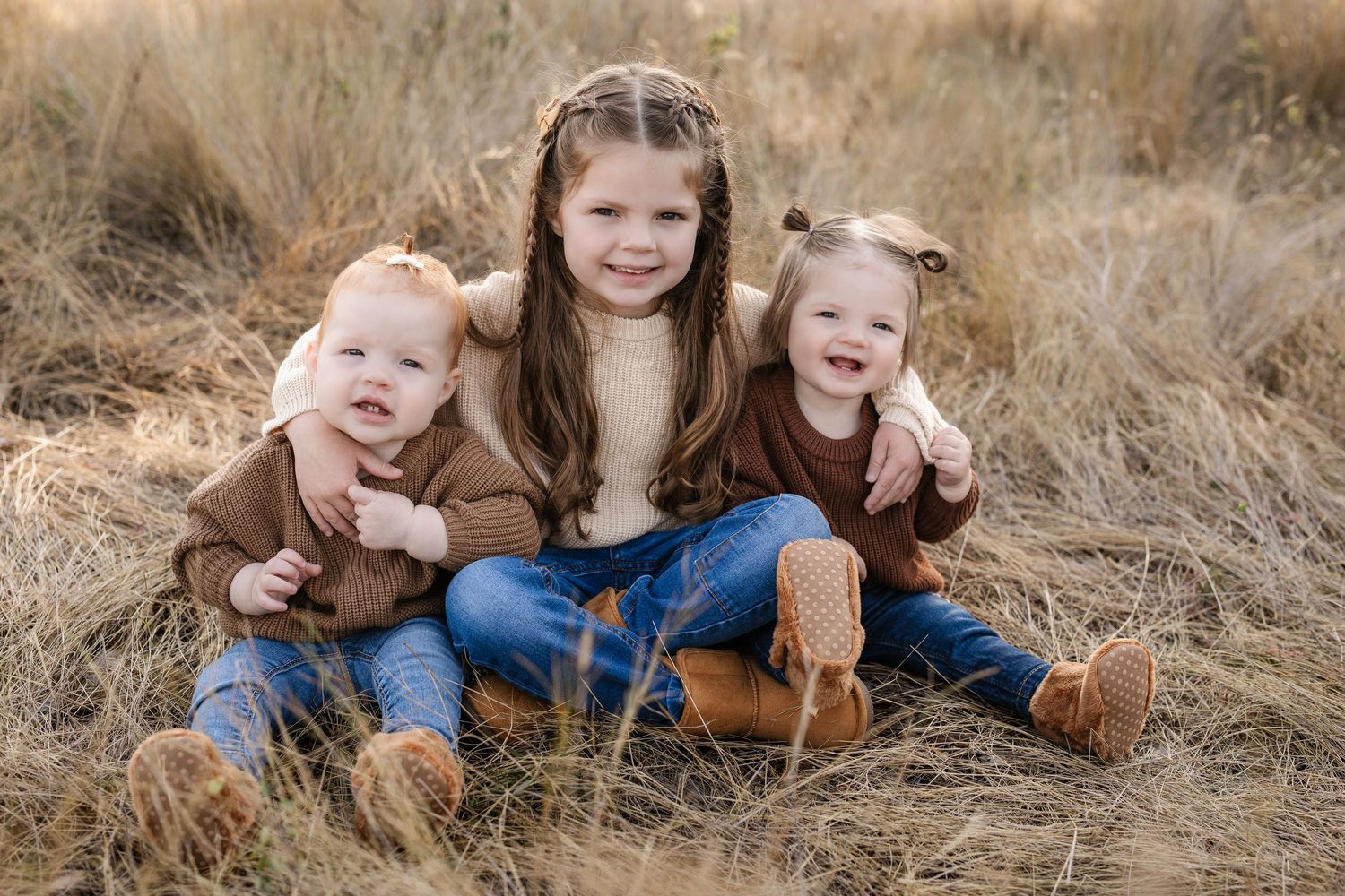 Family lying together in golden grass field during sunset photoshoot.