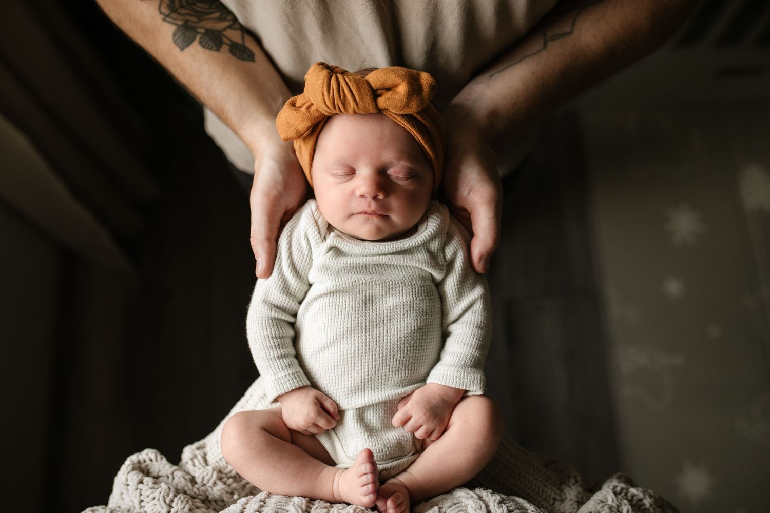 Black and white portrait of newborn baby being held against dark background.