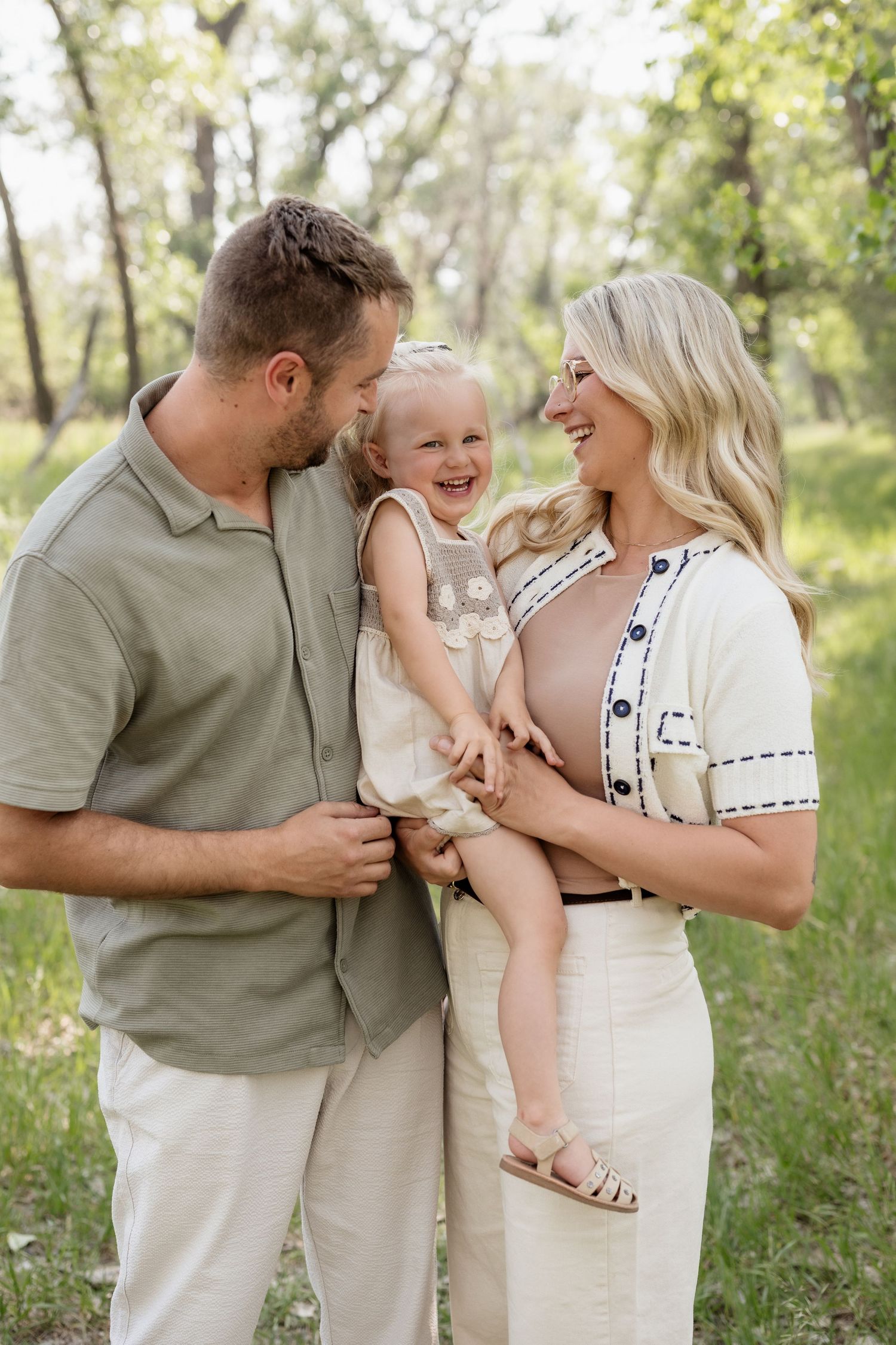 Family portrait sequence in coordinated neutral outfits enjoying playful moments in a sunlit field.