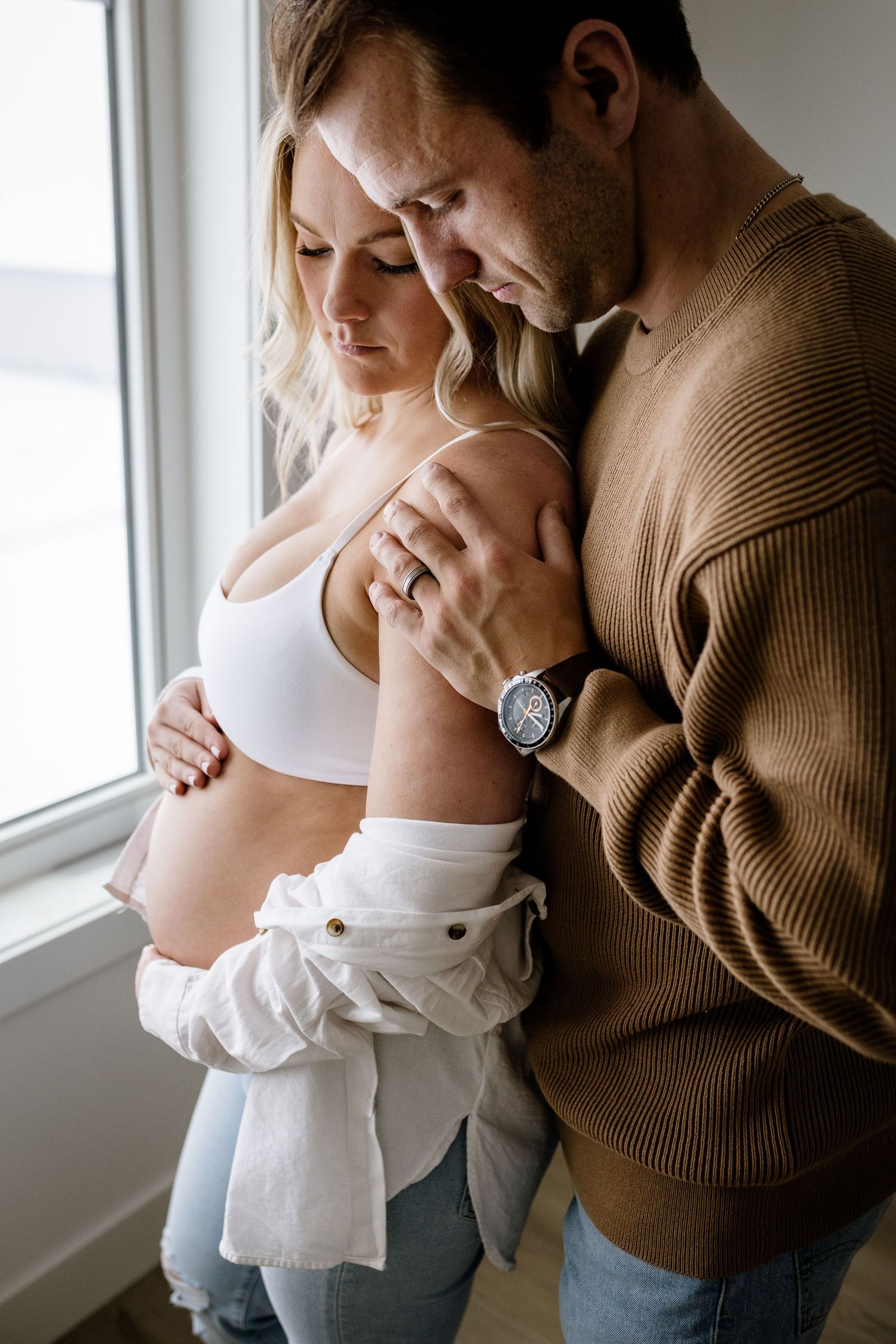 Tender maternity moment captured by window in natural light.