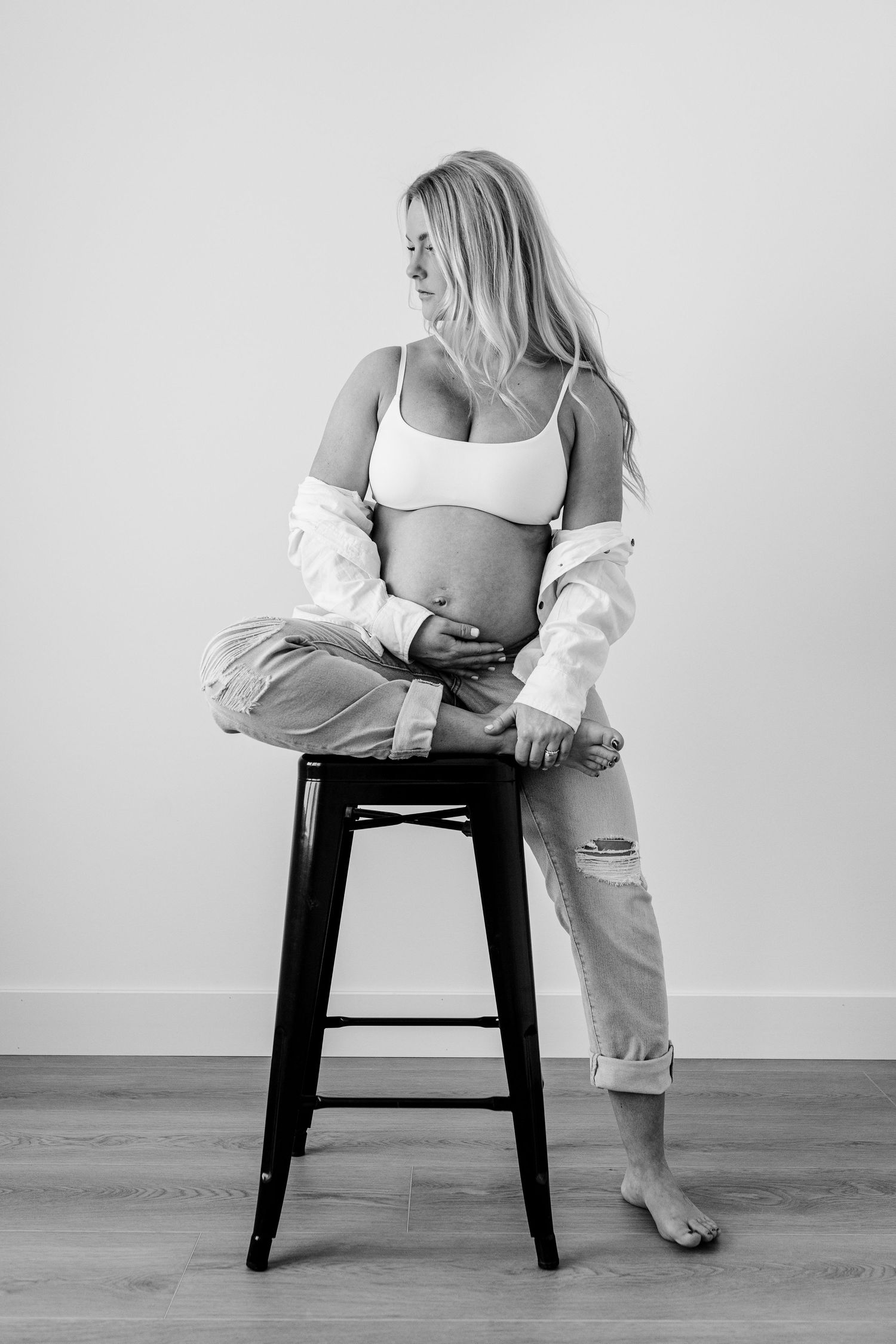 Black and white artistic photo series showing person in white outfit sitting on dark wooden stool in minimalist setting.