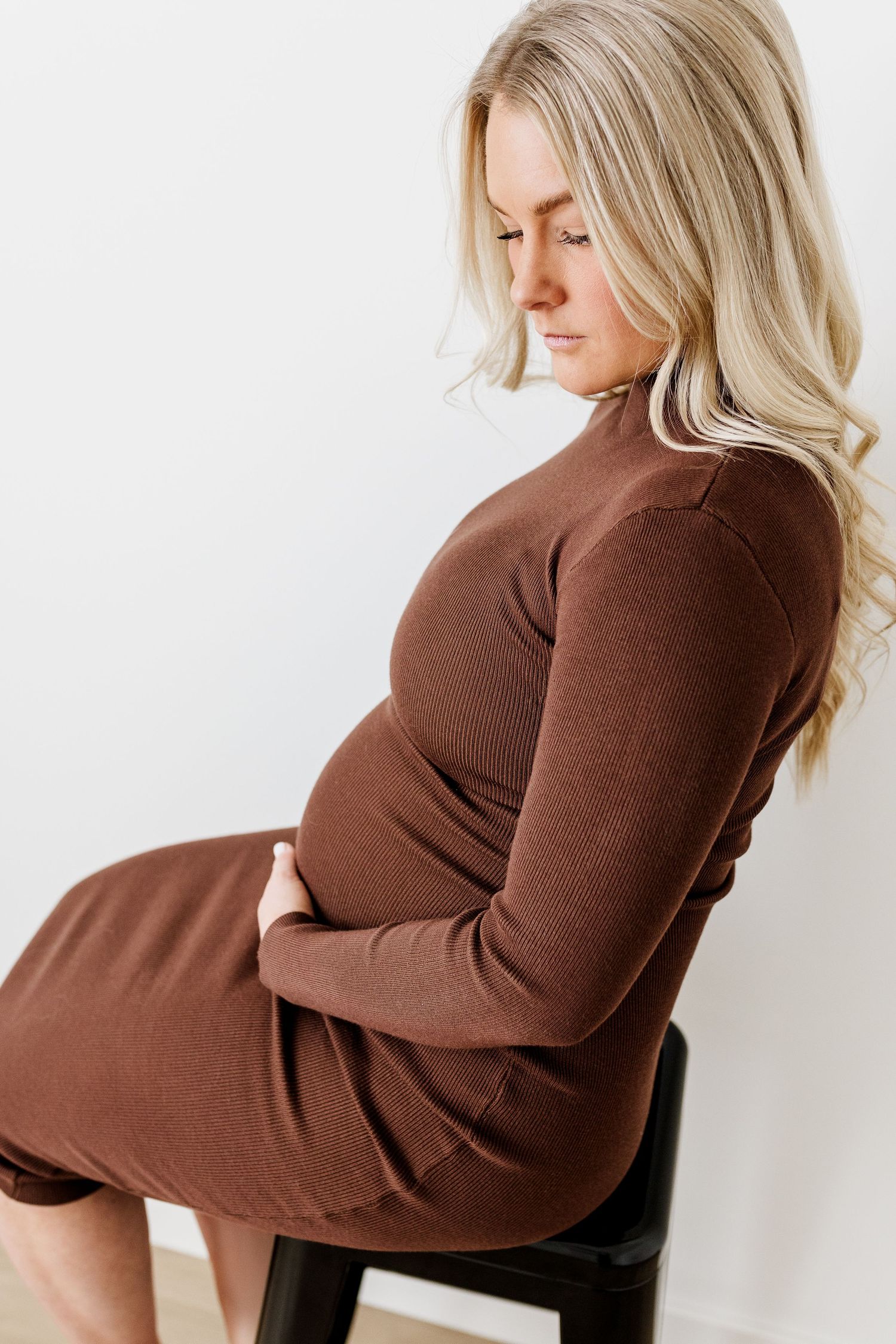 Maternity photo series showing woman in brown dress seated on chair.