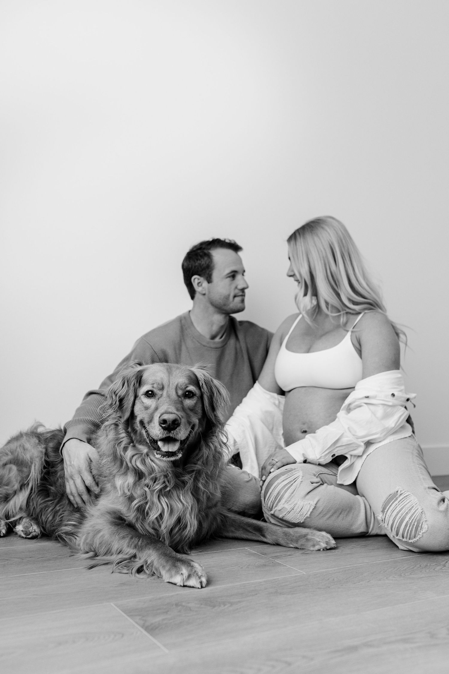Couple relaxing on floor with their golden retriever in black and white photography.
