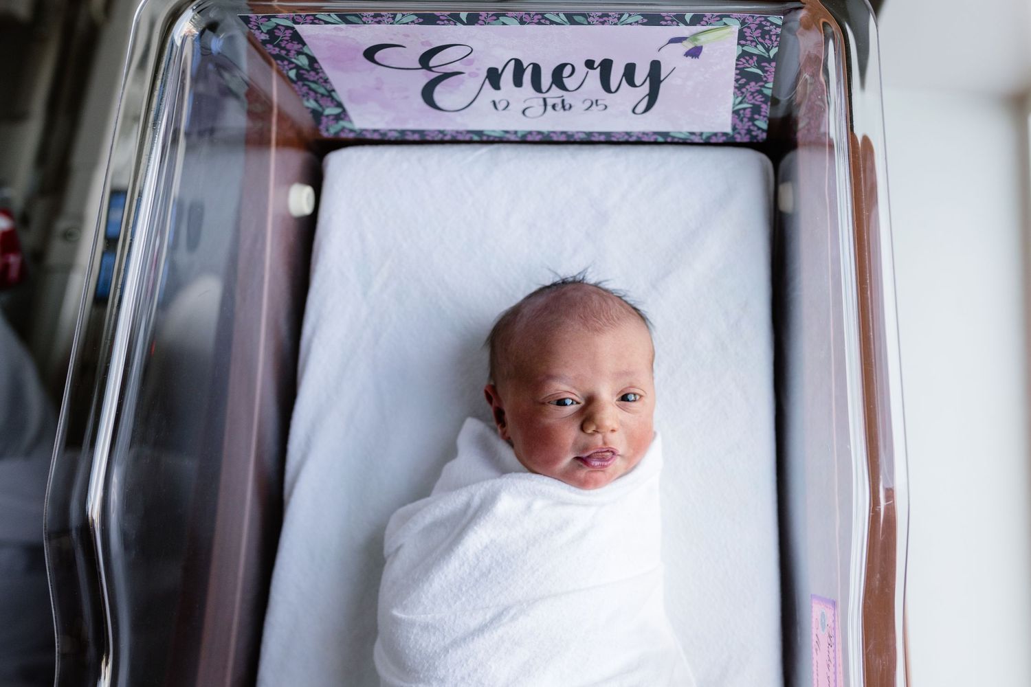 Newborn baby photographed in wooden frame with name display.