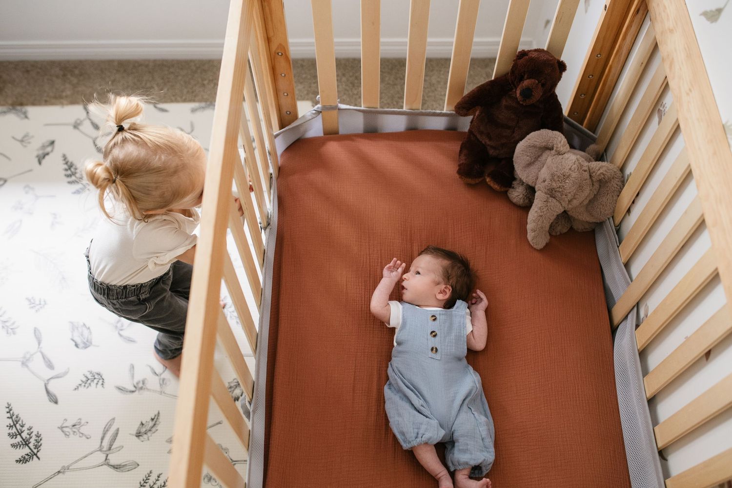 A wooden crib with floral patterned bedding and stuffed animals.