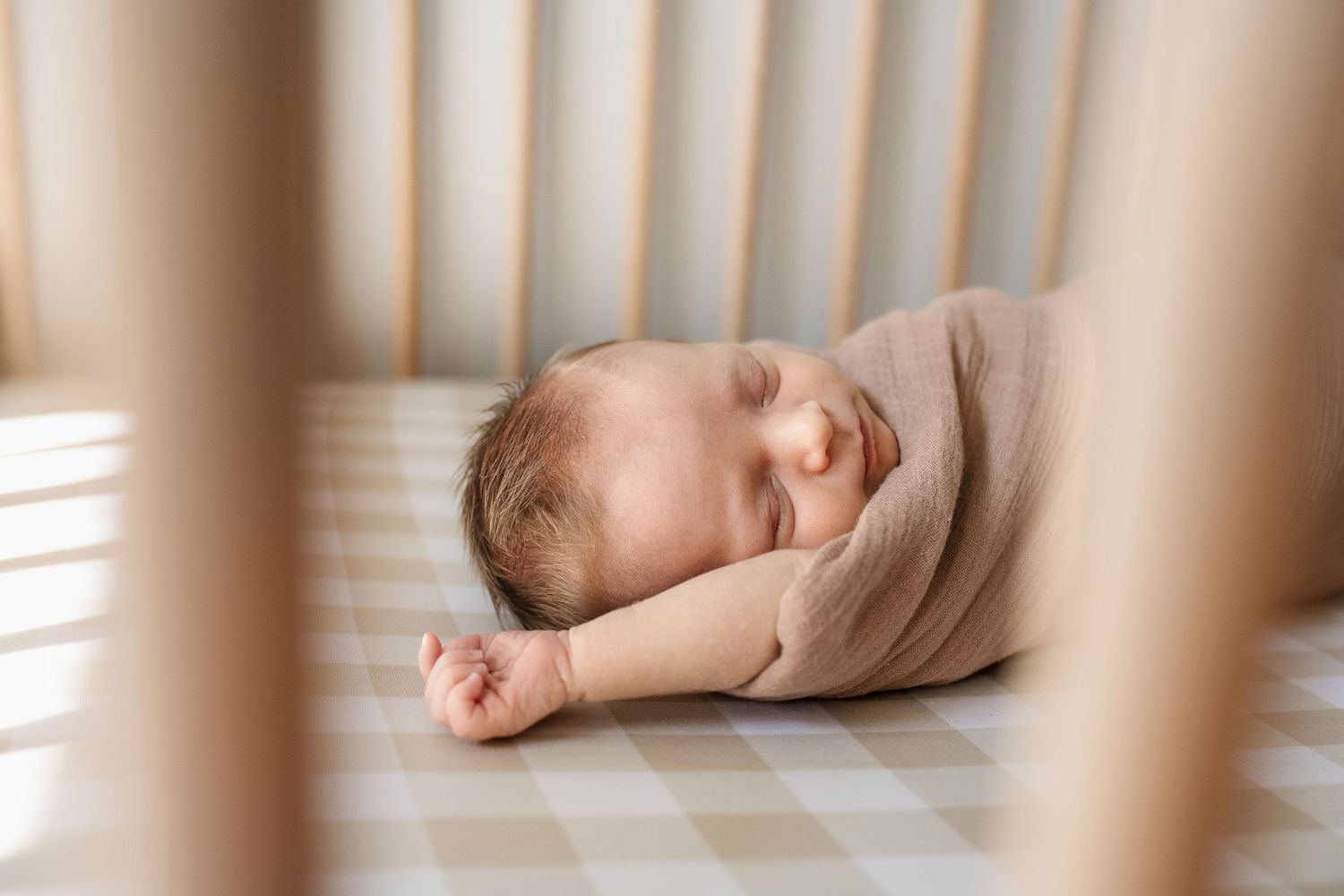 Peaceful sleeping baby in crib wrapped in soft beige swaddle.
