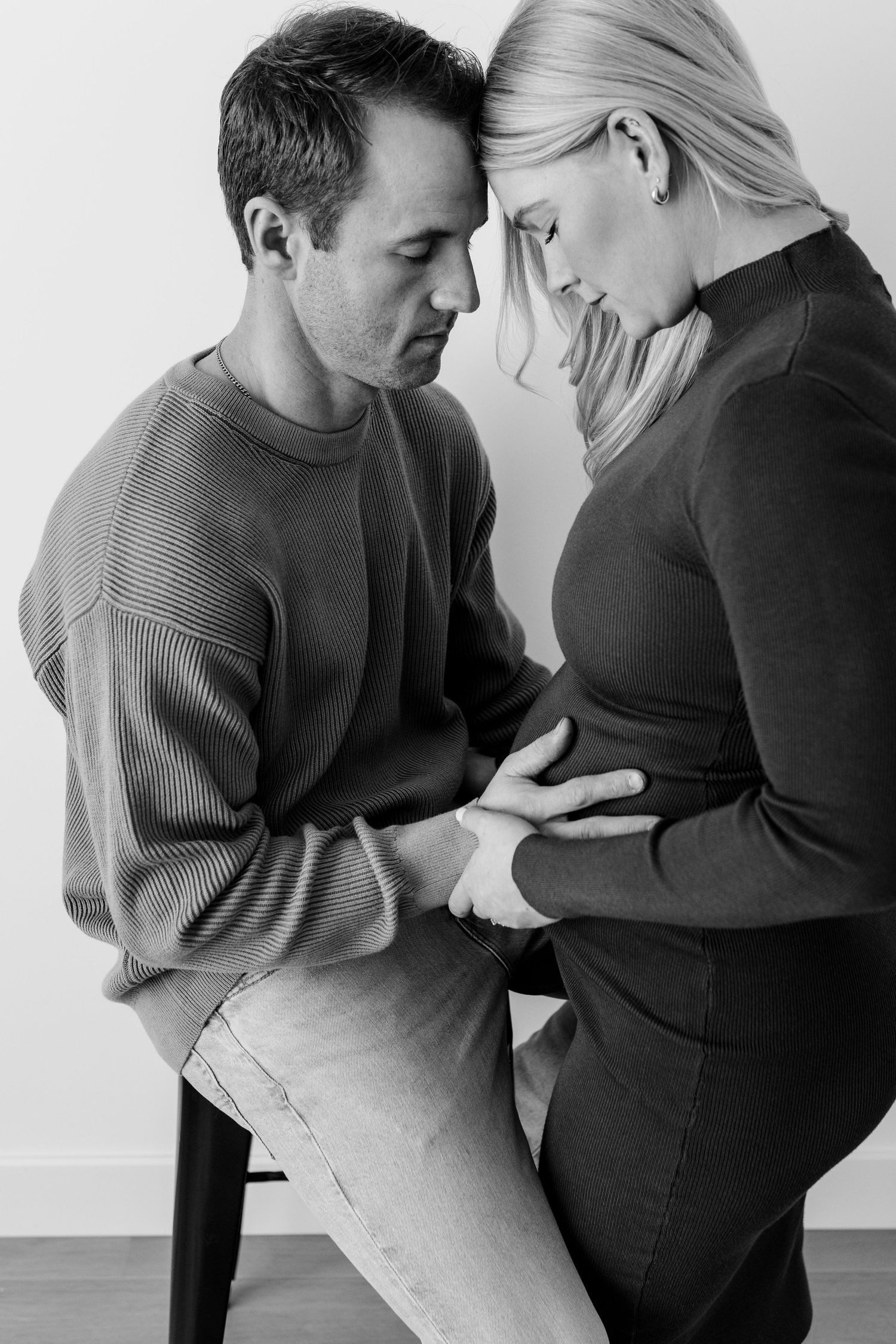 Black and white photo of an intimate moment between couple during pregnancy, with hands tenderly placed on baby bump.