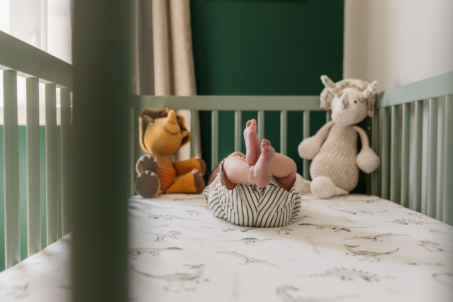 Nursery interior with white crib filled with plush toys against green and white walls.