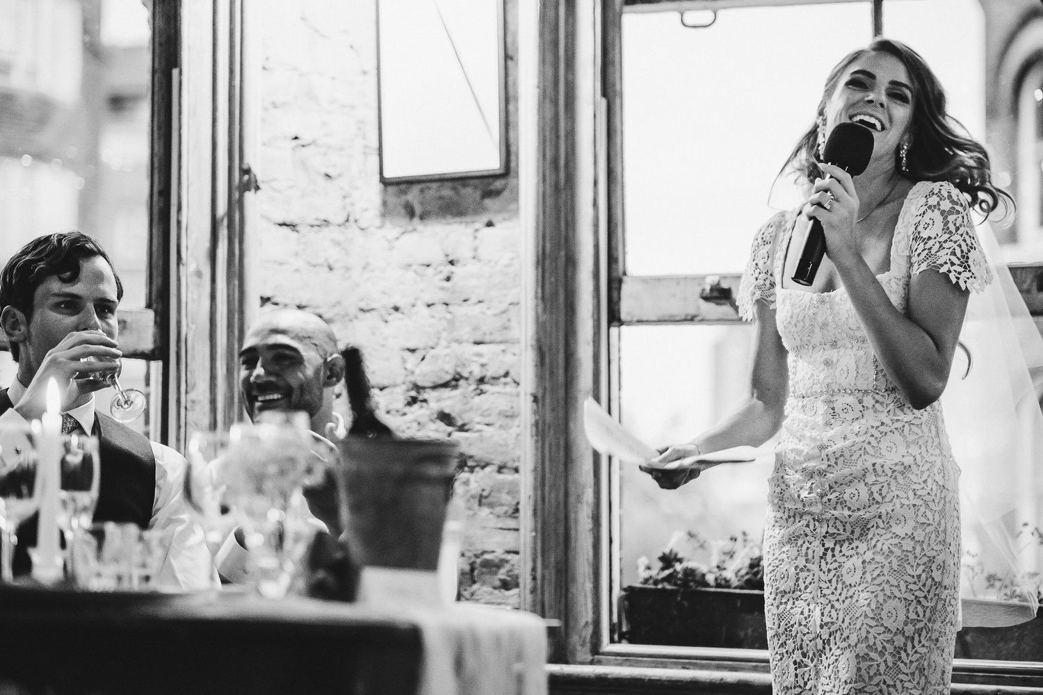 Black and white candid photos show wedding guests enjoying a reception through window frames.