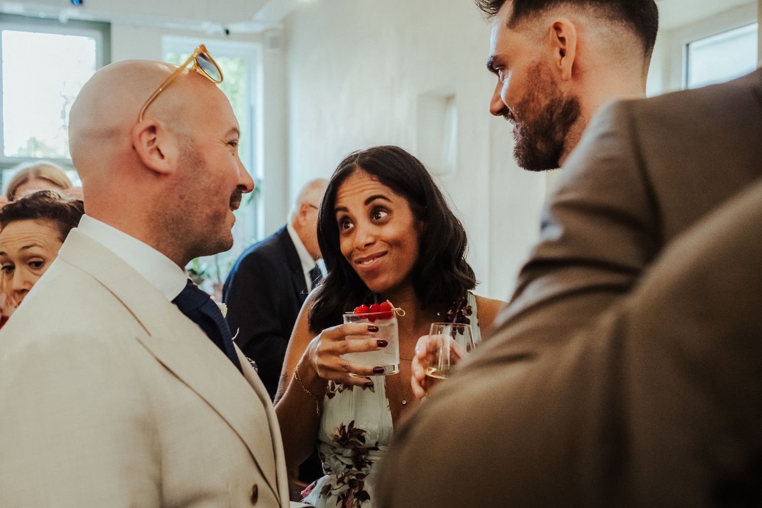 A group of guests engage in conversation while holding cocktails at an indoor social gathering.
