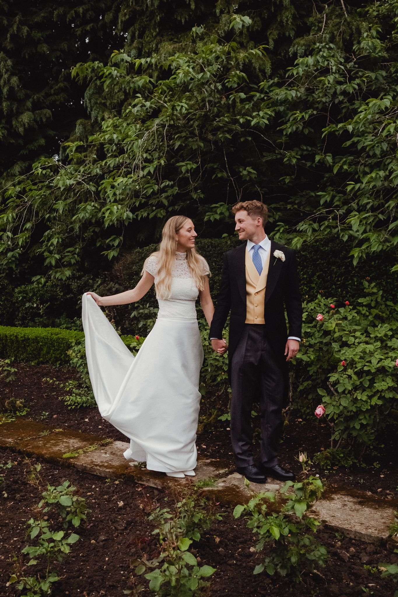 Two newly married people dance and twirl together on garden stone steps surrounded by lush greenery.