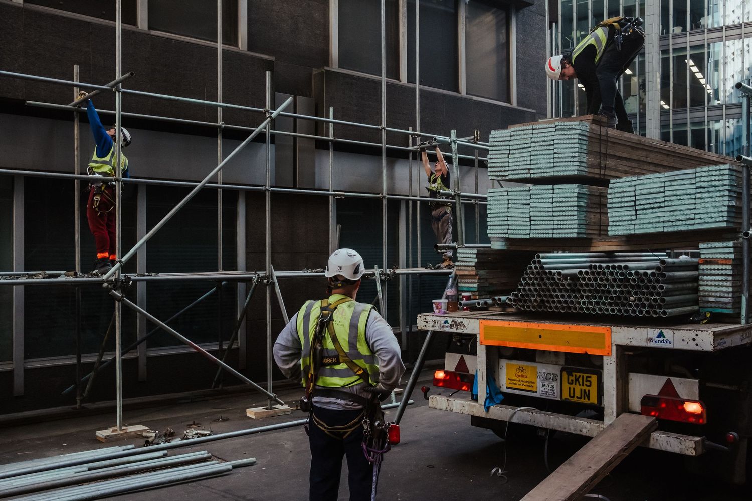 Construction workers in safety vests and hard hats install glass panels on a modern building facade.