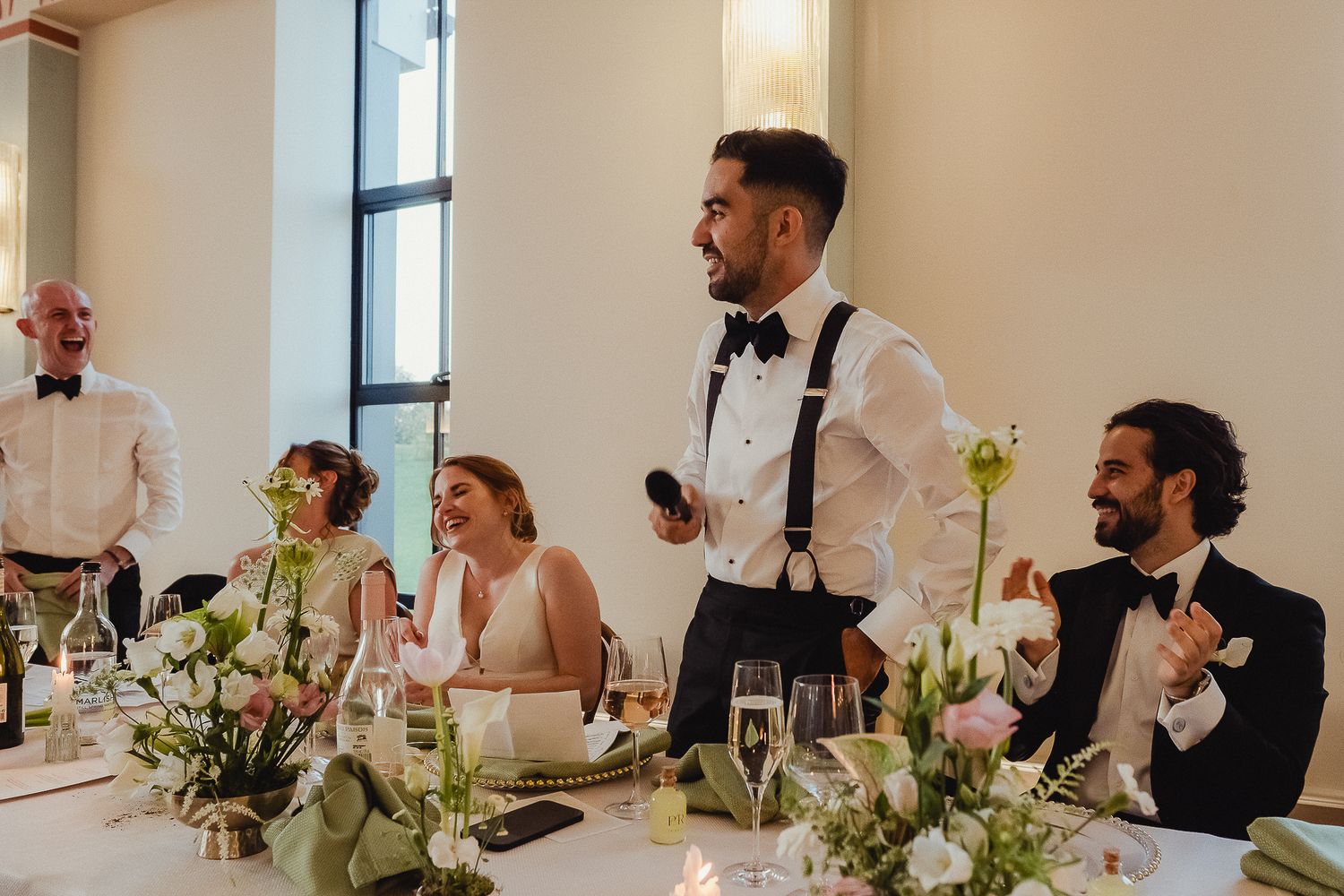 Wedding guests seated at long tables decorated with floral centerpieces and white linens during an elegant reception.
