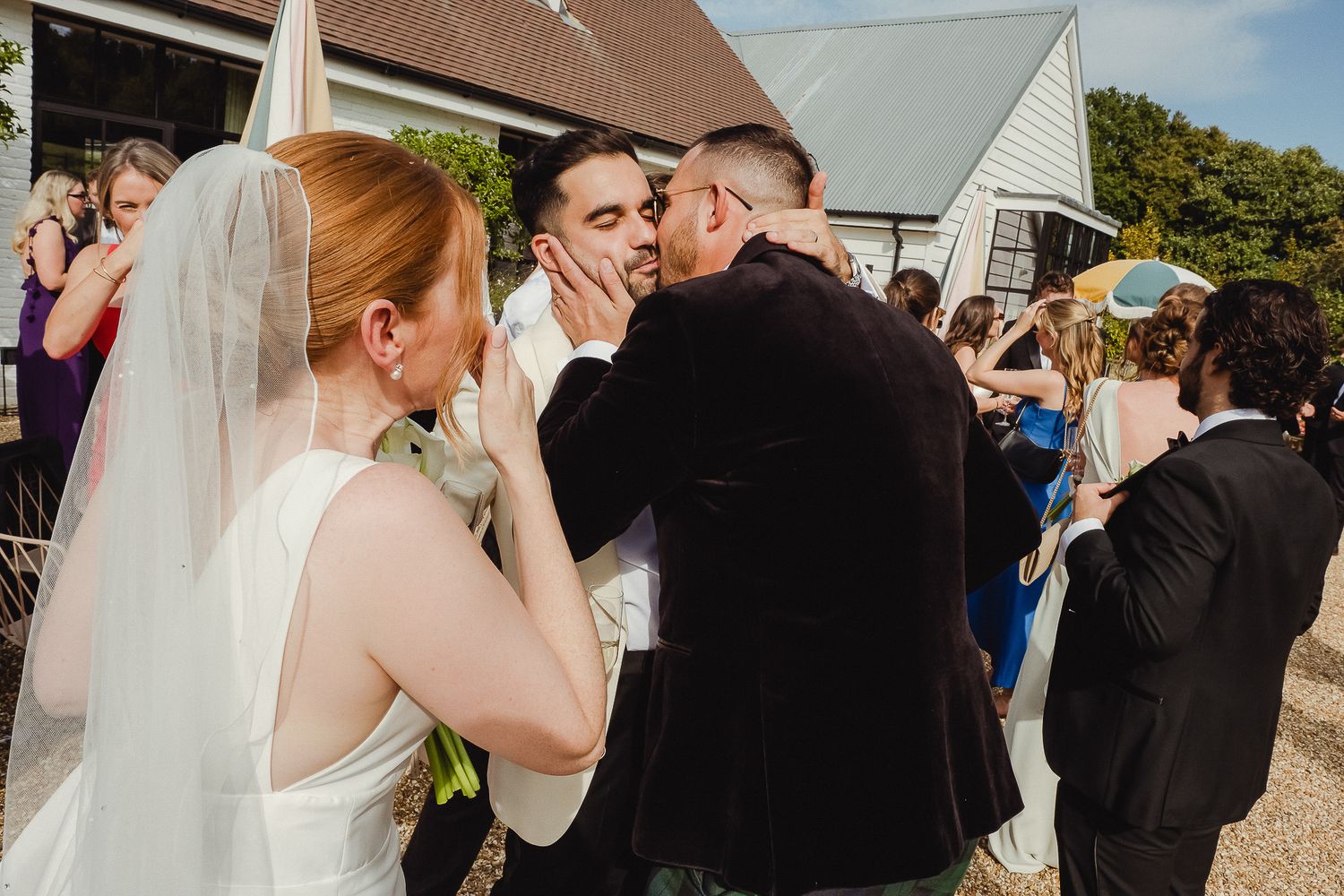 Wedding guests gather outdoors on a sunny day to celebrate and take photos at a rustic venue.