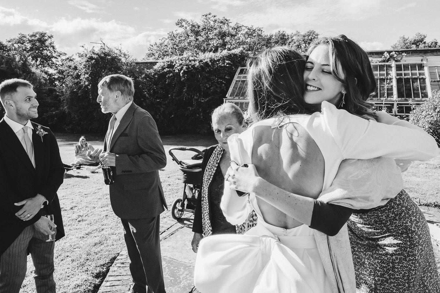 Wedding guests enjoy candid moments during an outdoor celebration with multiple couples dancing and embracing.