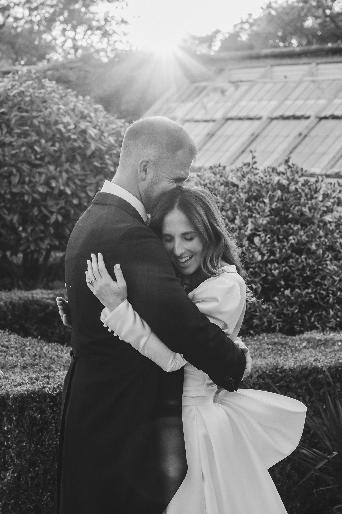 Black and white wedding portraits show intimate moments between couple in sunlit garden setting.