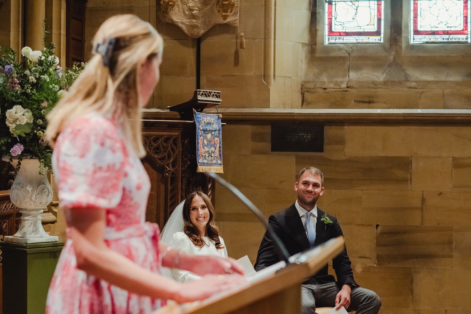Wedding guests seated in wooden church pews during an indoor ceremony with natural lighting.