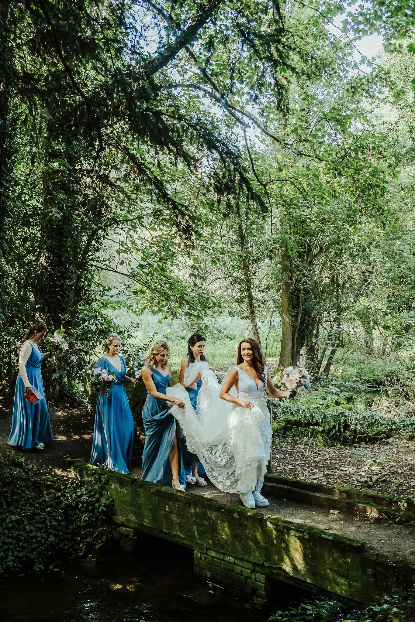 Wedding party walking along a scenic wooded path under green leafy trees.