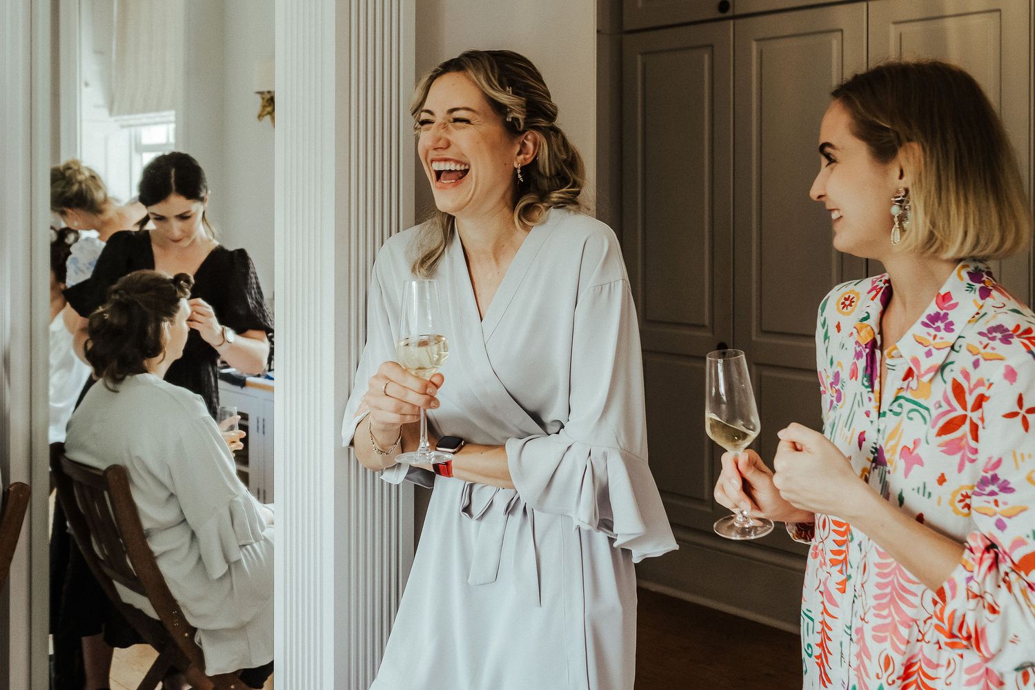 Wedding morning scene with people in robes sharing champagne and laughter.