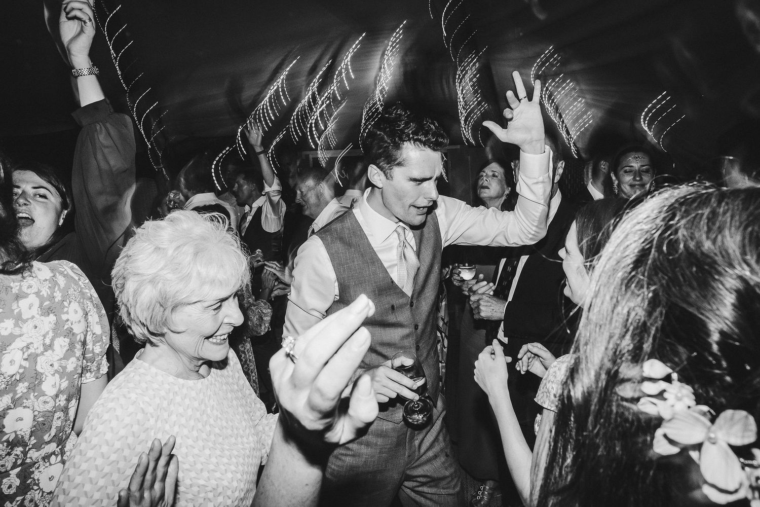 Black and white photo of people dancing and celebrating at a lively wedding reception.