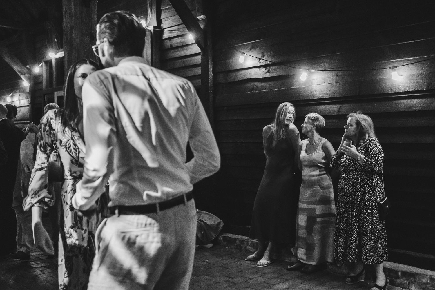 Black and white candid shot of people dancing at a wedding reception in a dimly lit venue.