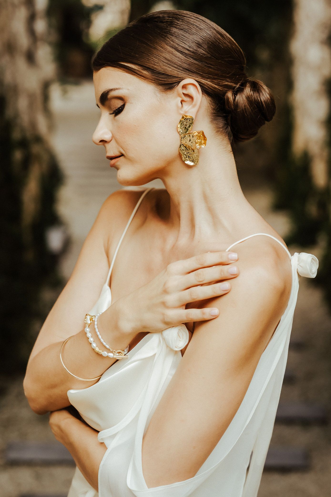Elegant bridal portrait series showcasing pearl jewelry and a classic white gown against a natural backdrop.