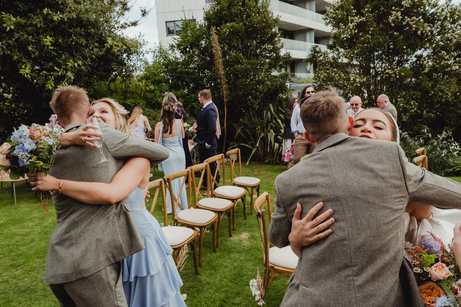 Guests celebrate with joyful dancing and embraces at an outdoor garden wedding reception.