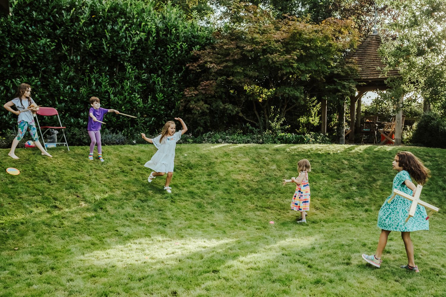Children play and dance on a sunny green lawn during an outdoor celebration.
