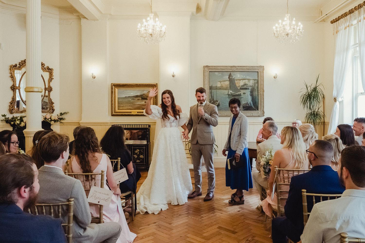 Elegant wedding celebration in a bright indoor venue with crystal chandeliers and classic decor during a reception toast.