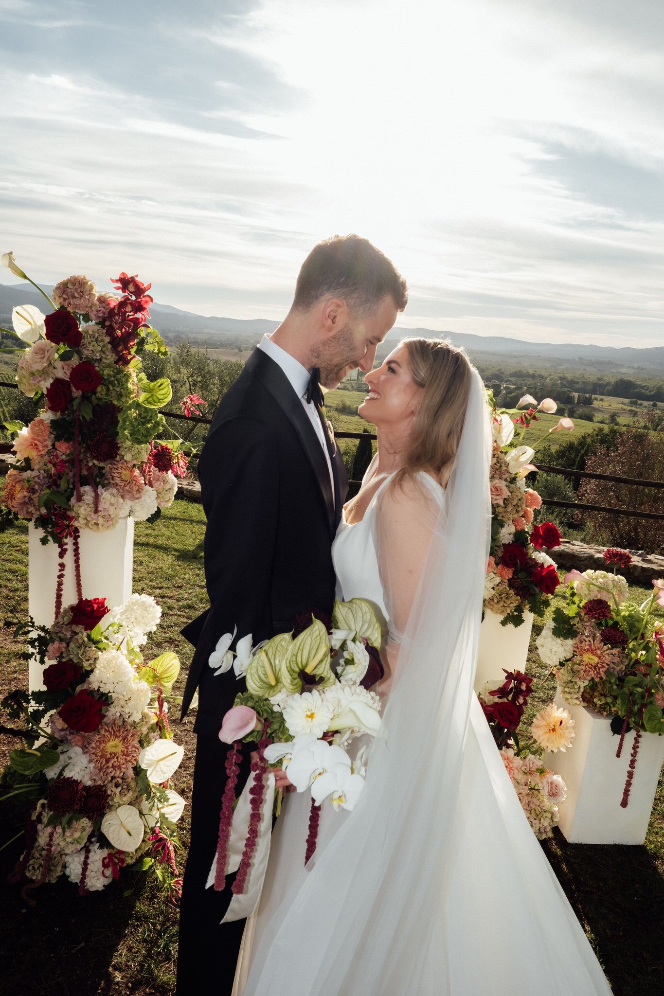 Bride and groom share an intimate moment at an outdoor wedding ceremony surrounded by lush floral arrangements with a scenic valley view.
