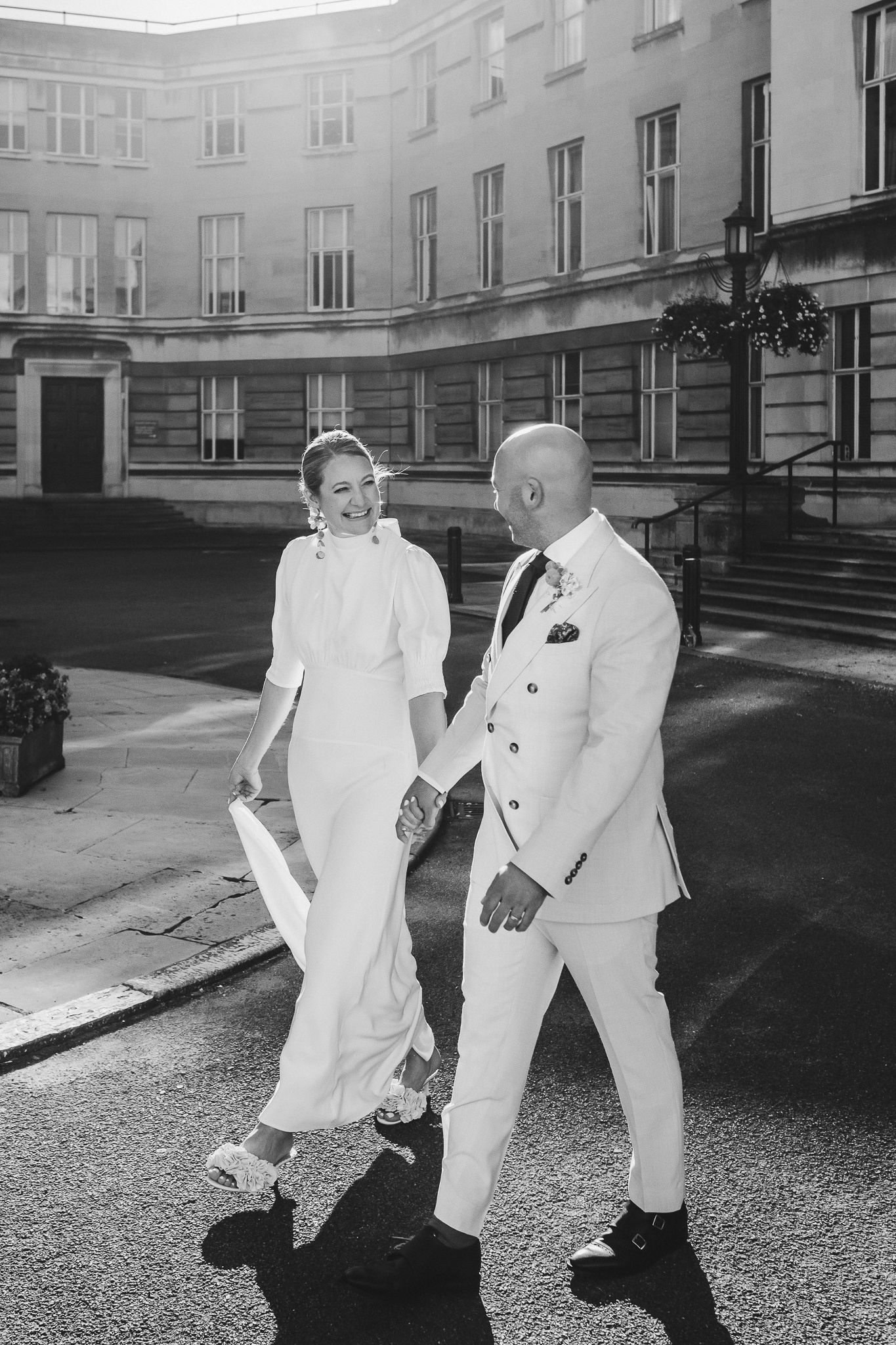 Two people in crisp white outfits walk together in a black and white photo of a historic courtyard.