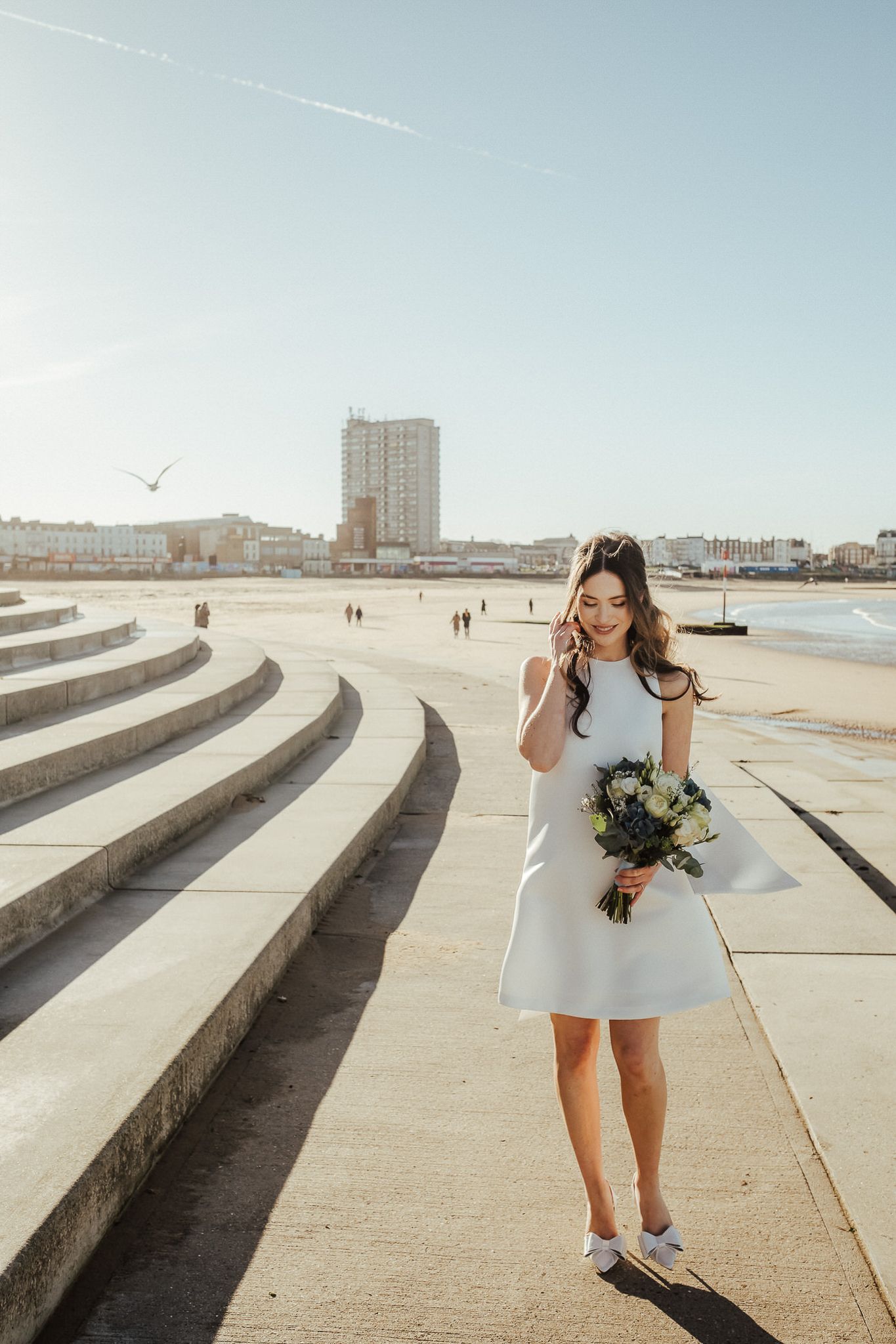 A series of images showing a person in a white dress walking along curved concrete steps at a beach on a sunny day.