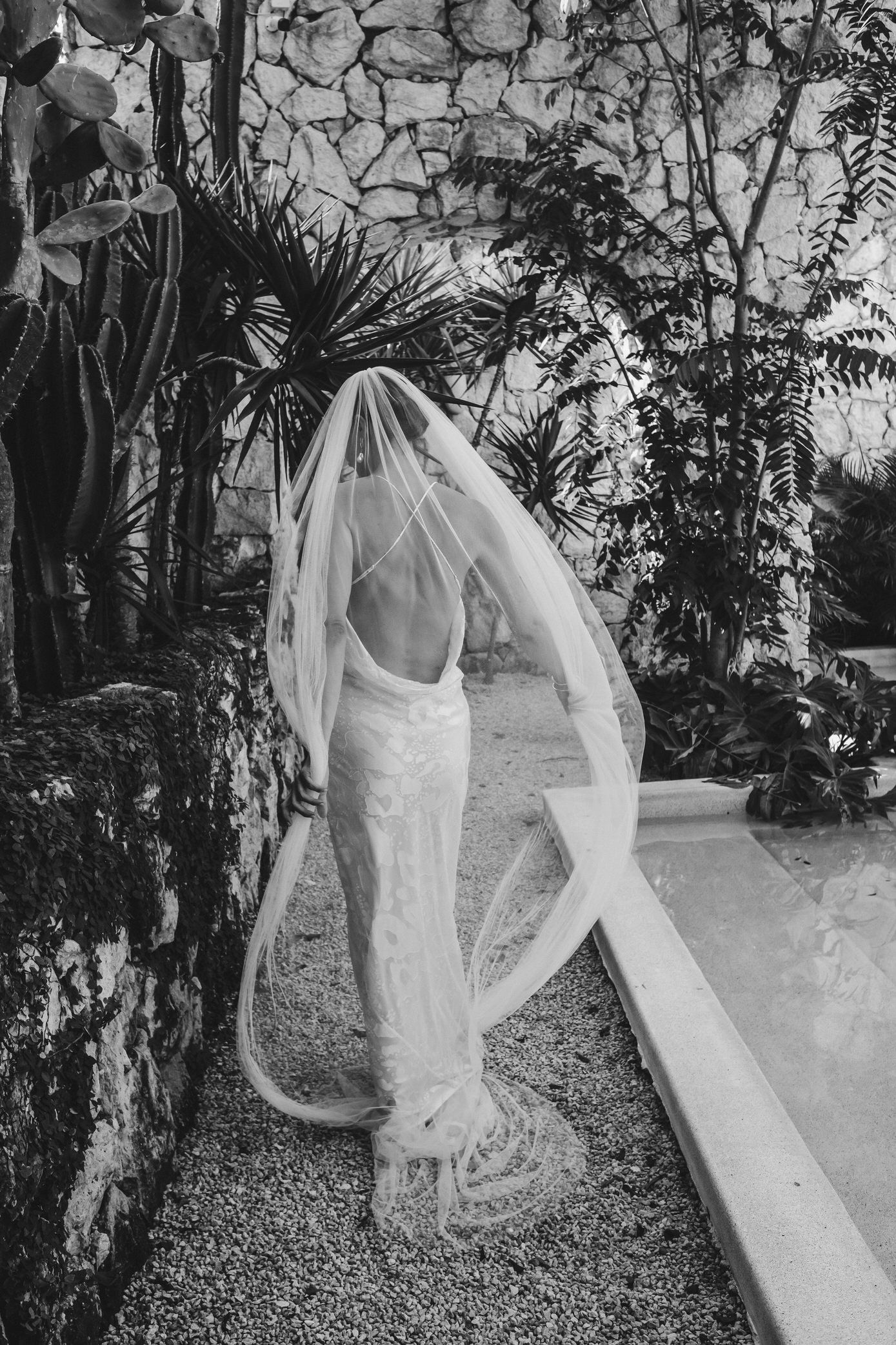 Wedding dress displayed in a lush garden setting with stone walls and tropical foliage creating a romantic atmosphere.