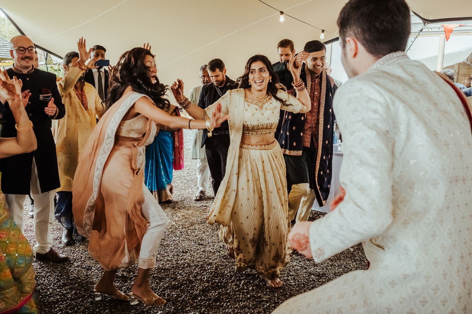 Wedding guests dancing under a tent in traditional fusion Indian and Western attire.