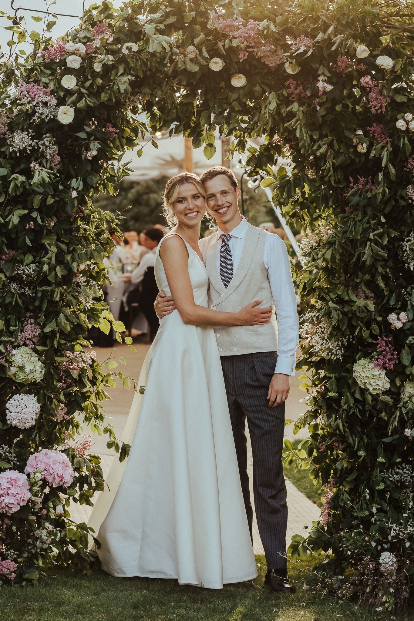 White-clad flower girls walk through a garden adorned with blooming roses and delicate string lights.