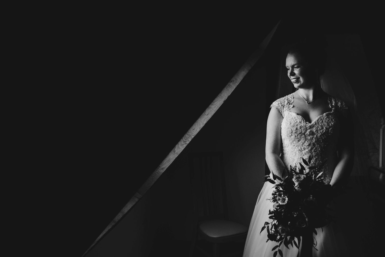 Dramatic black and white portrait of bride holding bouquet in window light.