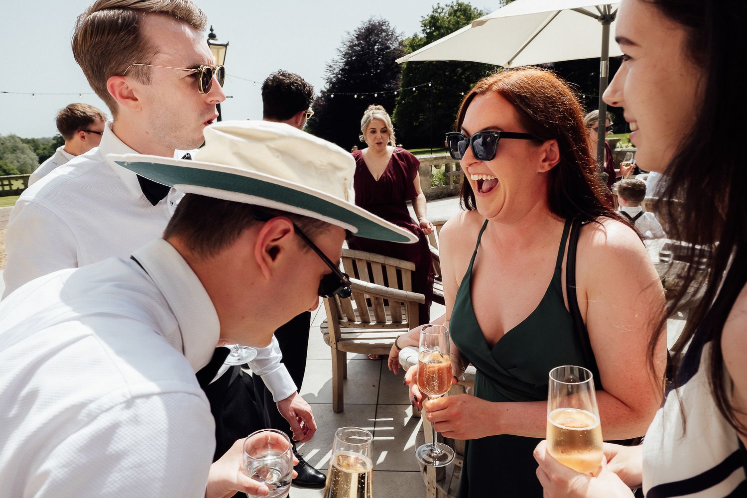 Group of elegantly dressed guests enjoying champagne at an outdoor summer garden party event.