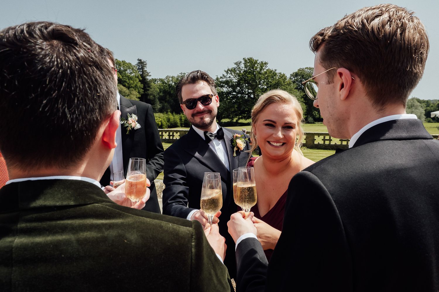 Group of elegantly dressed guests toasting with champagne glasses at an outdoor wedding reception.