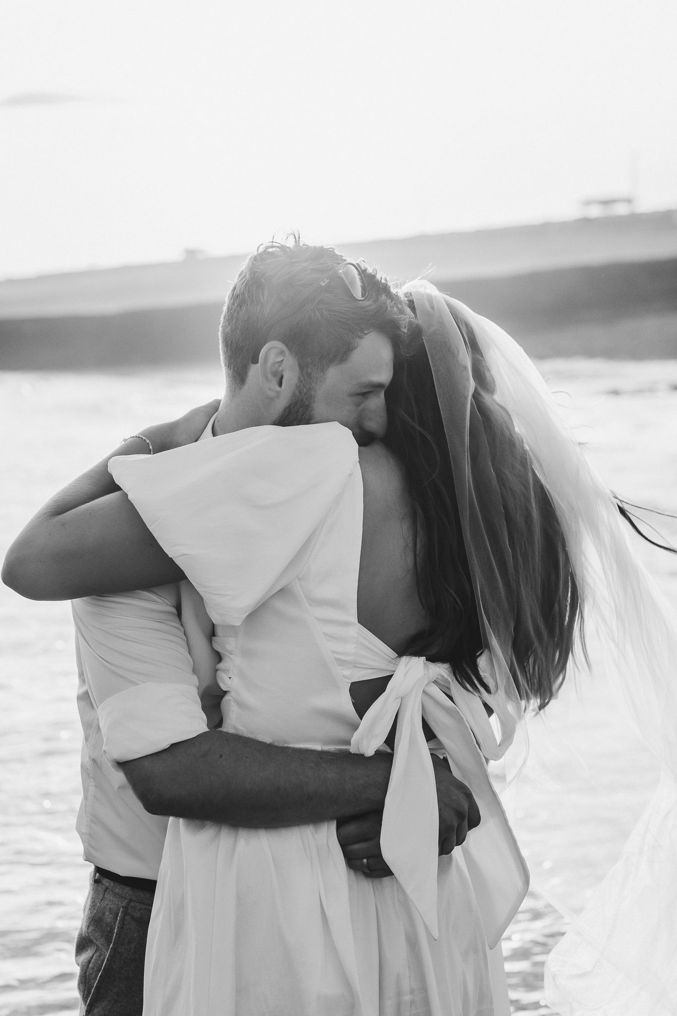 A couple embraces on a beach during sunset in a romantic black and white photograph.