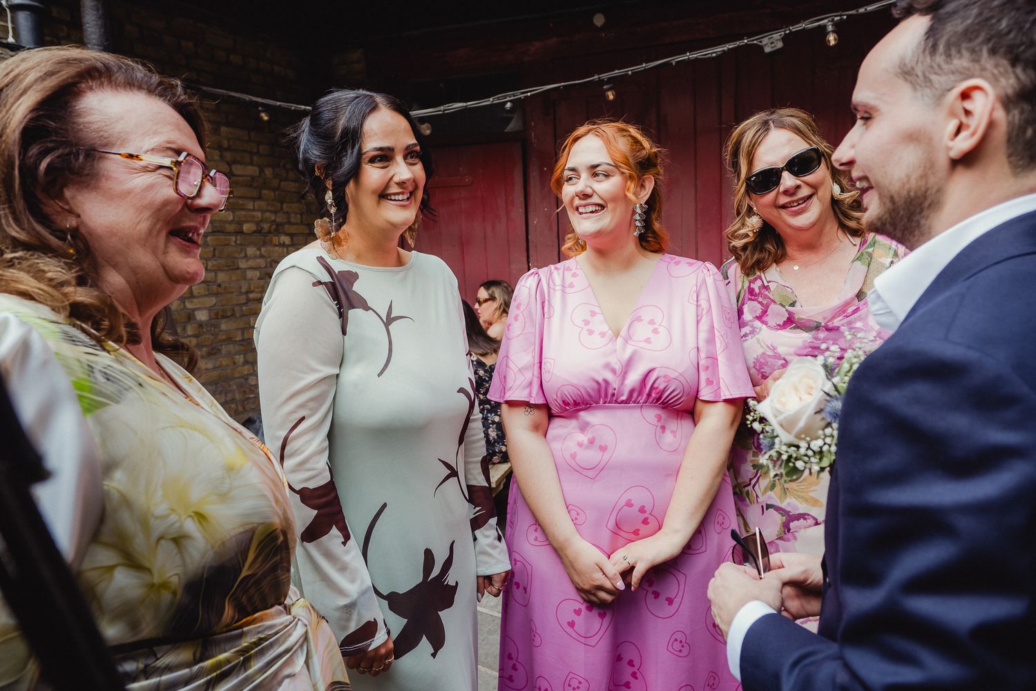 Wedding party laughs together while standing in a row wearing pink and sage green attire at outdoor celebration.