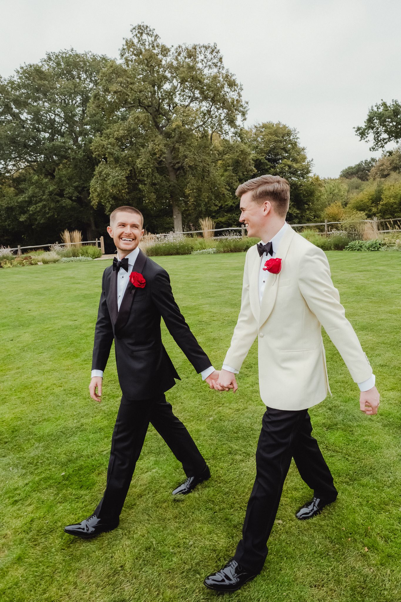 Two people in formal attire playfully dance and spin together on a green lawn with trees in the background.