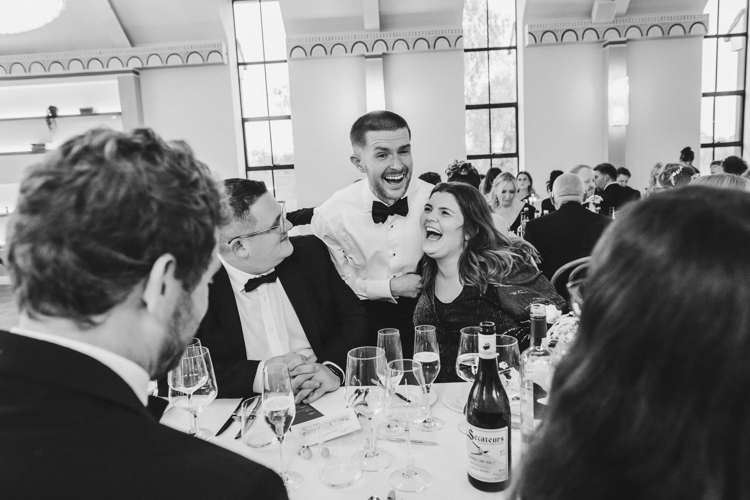 A group of people gather around tables at a formal dining event, laughing and socializing together.