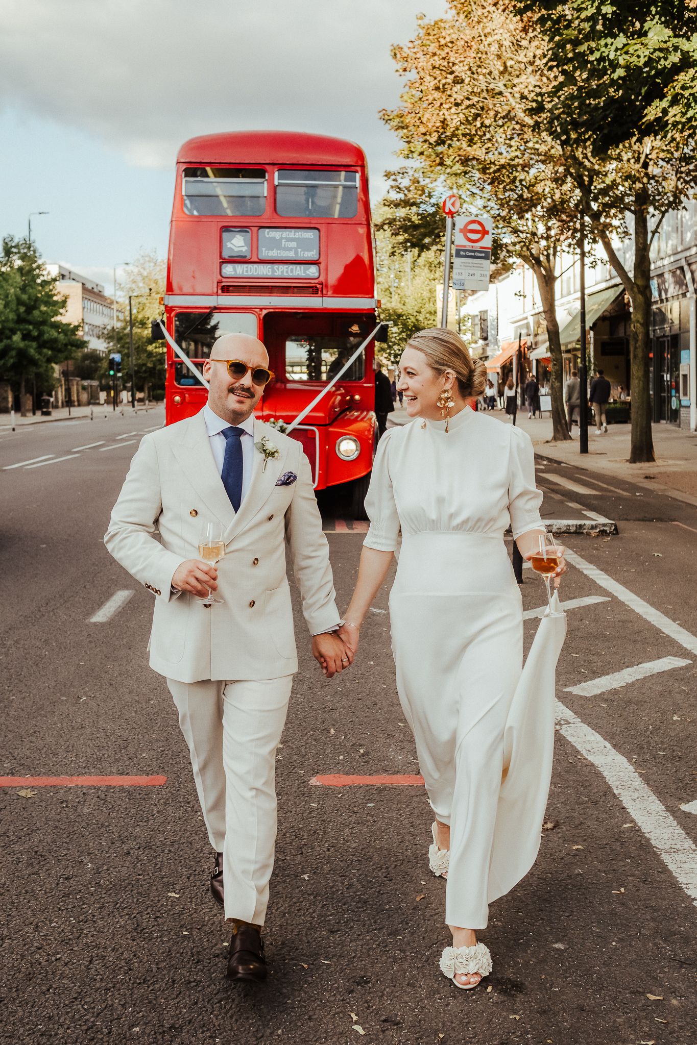 A couple in matching white outfits walks down a London street with an iconic red double-decker bus in the background.