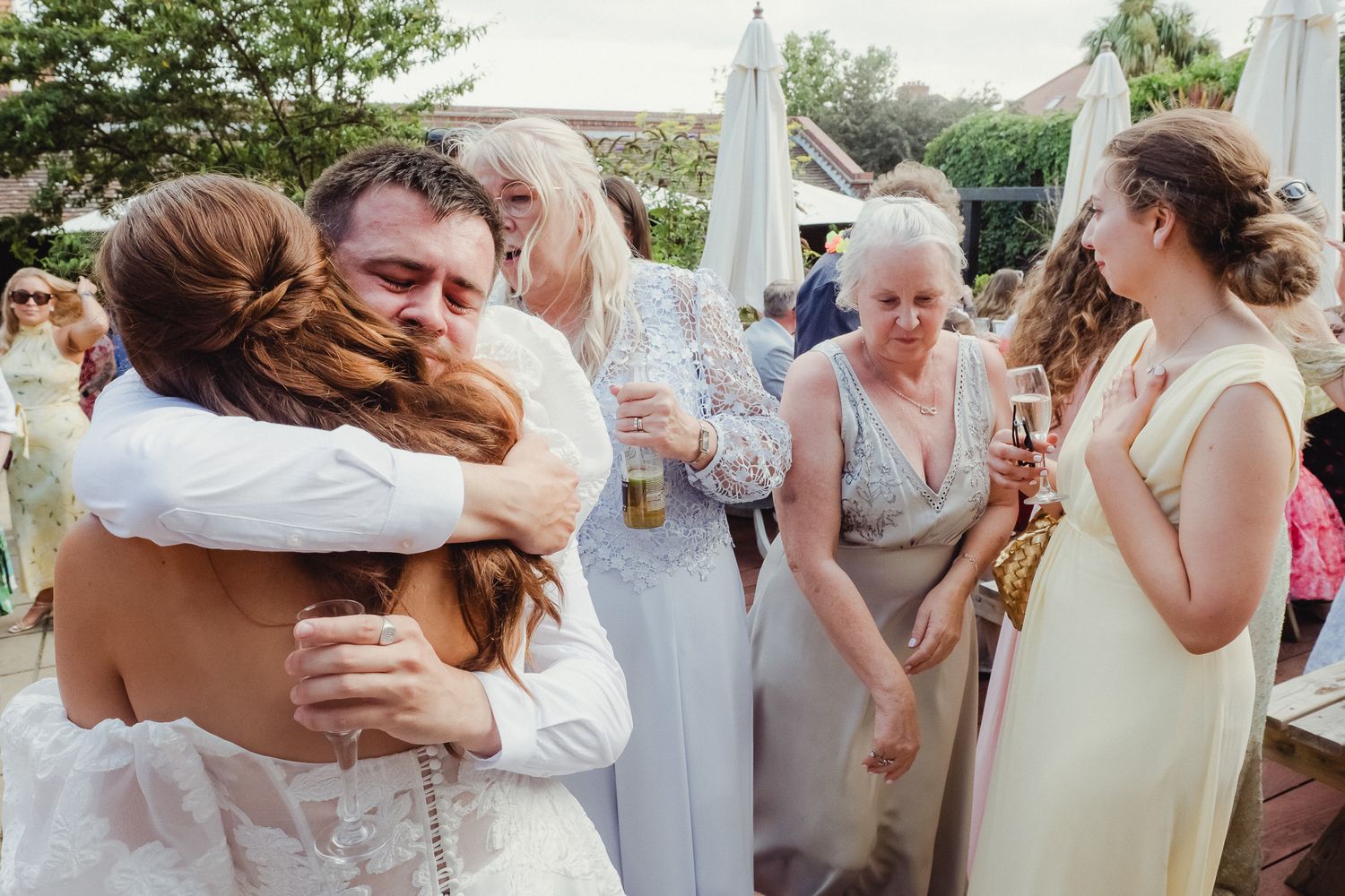 A series of candid wedding moments showing guests hugging and celebrating at a brick-walled venue.