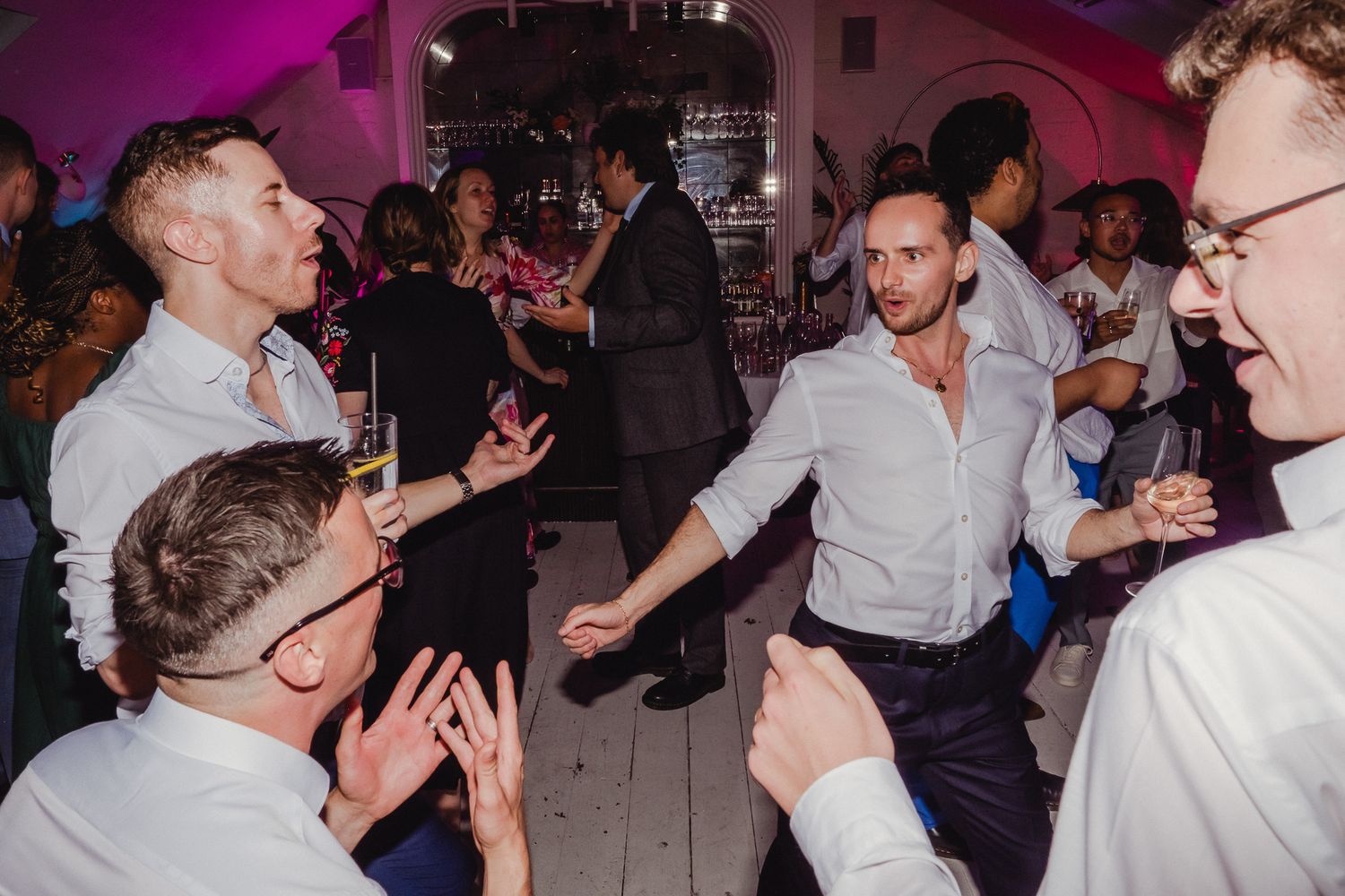 People dancing and socializing at a nightclub with purple lighting and festive atmosphere.